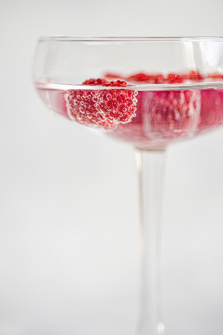 Transparenter glatter Glasbecher gefüllt mit erfrischendem Cocktailsekt mit reifen frischen Himbeeren vor unscharfem Hintergrund