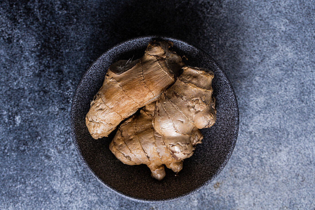 Black stone bowl with ginger roots on concrete kitchen table