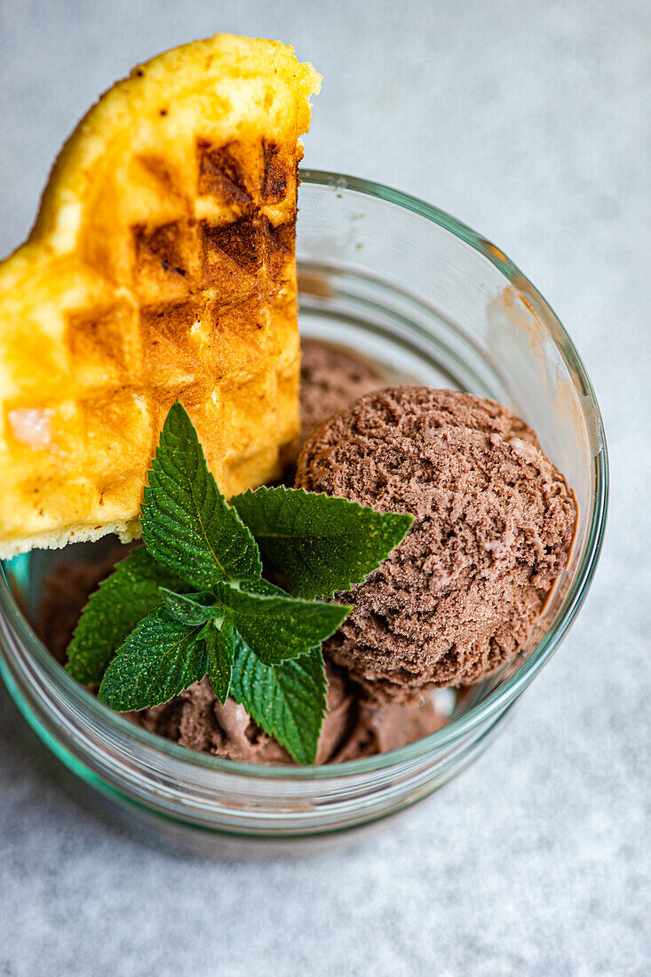 Top view of glass of homemade coffee ice cream with waffle and fresh mint on gray surface