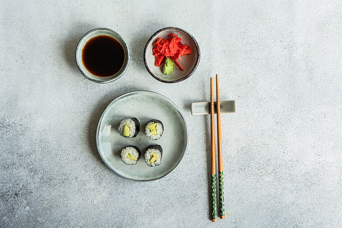 Blick von oben auf ein japanisches Essensset mit Avocado-Maki-Rolle und gebratenem Sushi mit Sojasauce und Ingwer auf einem weißen Betontisch