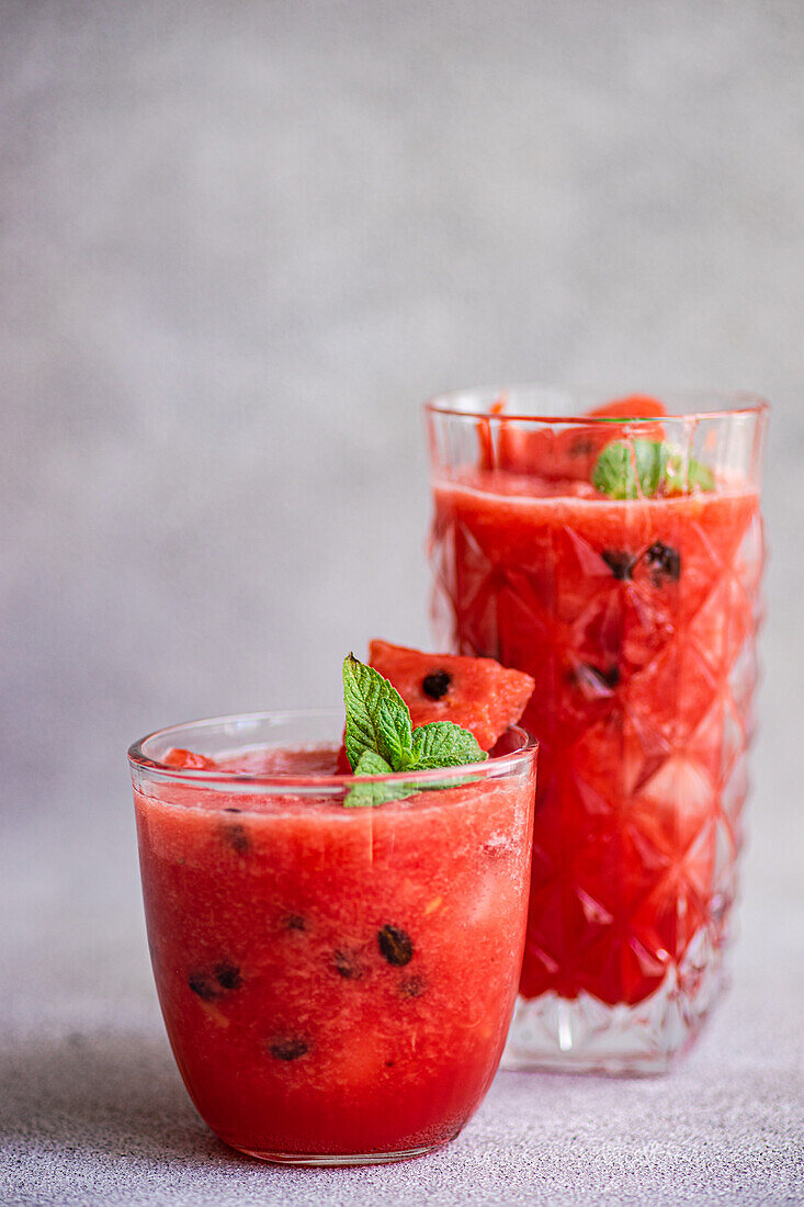 Gläser mit Margarita-Cocktail und Wassermelonen-Smoothie, garniert mit Minzblättern, auf einem grauen Tisch