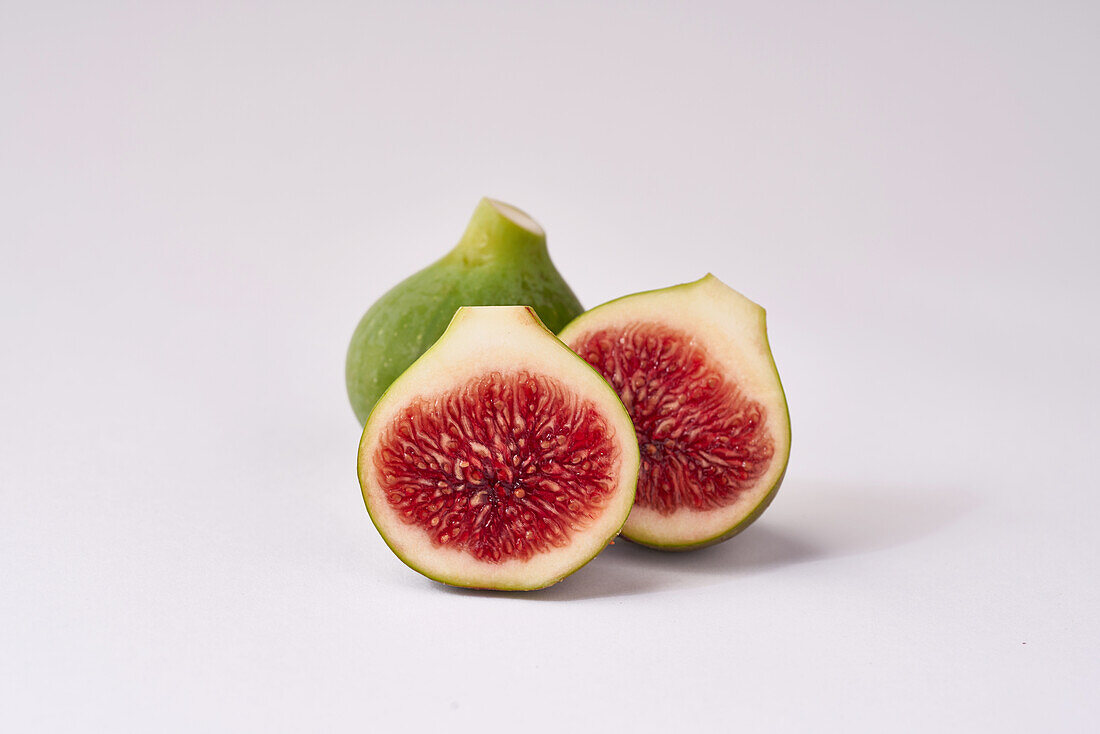 Ripe figs with one cut in half to reveal the juicy red interior, arranged against a clean, white backdrop.