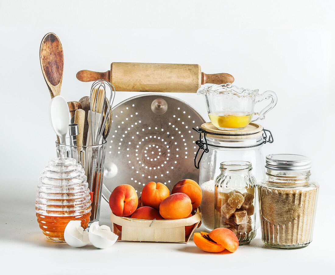 Backgeschirr mit Aprikosen, Küchenutensilien, Werkzeugen, Honig und Zutaten auf weißem Hintergrund. Backen mit Früchten der Saison zu Hause. Frontansicht