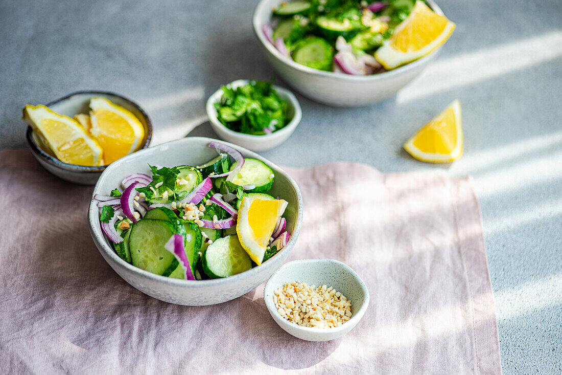 From above of healthy vegetables salads with organic cucumber, red onion, coriander and chopped nuts placed in a concrete table