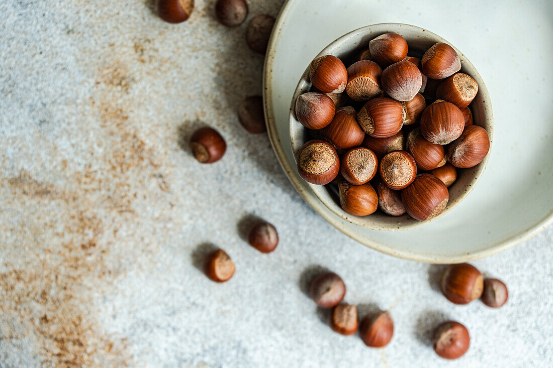 Top view of small bowl with fresh chestnuts placed on a plate with chestnuts scattered around the table