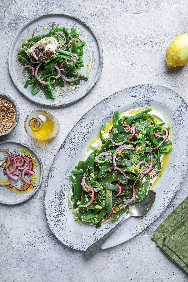 Draufsicht auf einen appetitlichen vegetarischen Salat mit grünen Kräutern und Zwiebelscheiben, der auf einem Teller mit Öl serviert und mit Zitronenschalen garniert wird