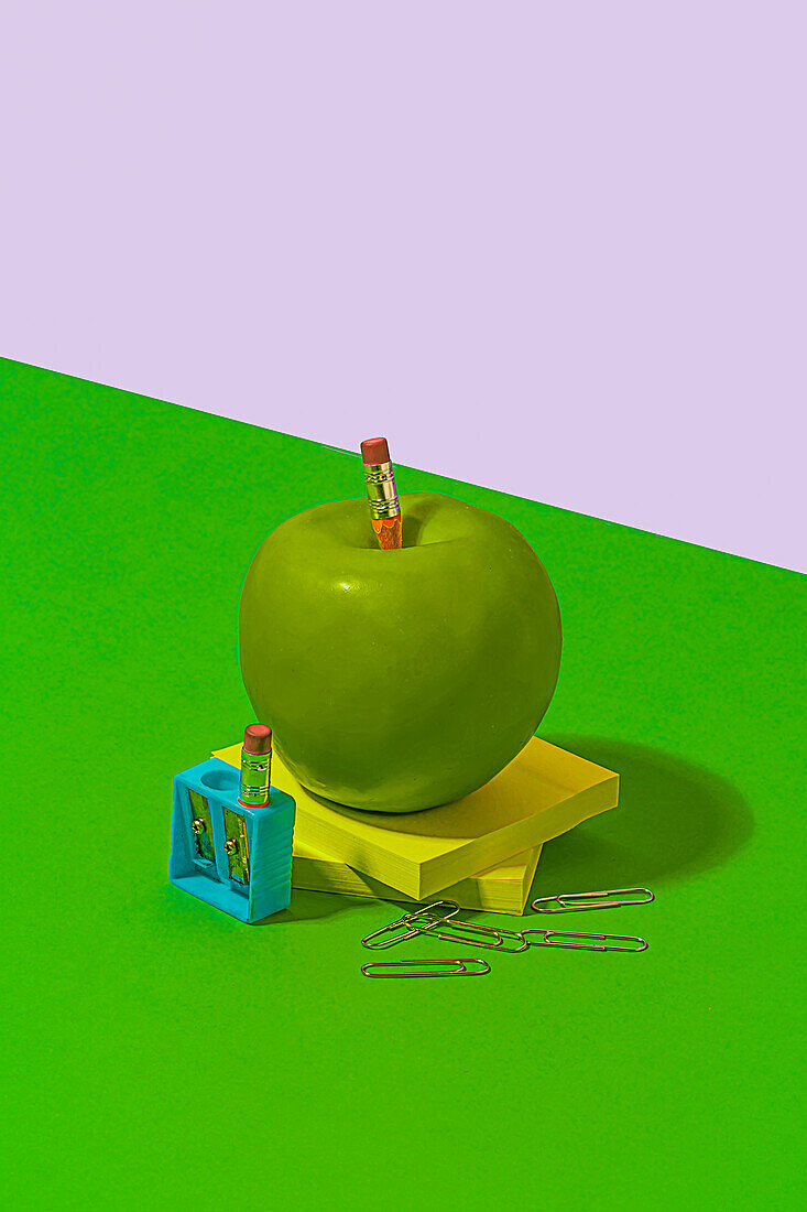 Granny Smith apple placed on sticky notes near office or school supplies on bright green and white background