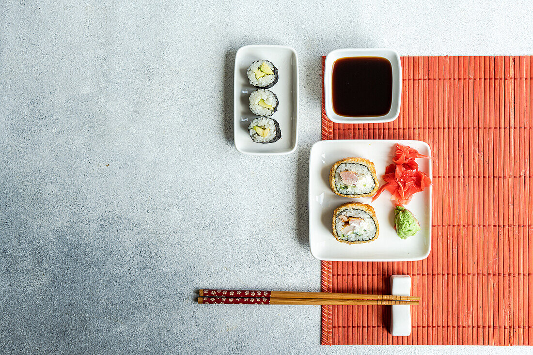 Verschiedene Sushi-Rollen auf Tellern mit Stäbchen und Sojasauce auf weißem Hintergrund von oben