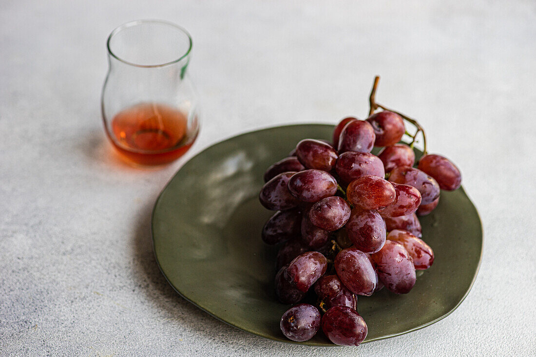 High angle of red Champagne grape variety served on dark plate near pink champagne wine in glass against gray background