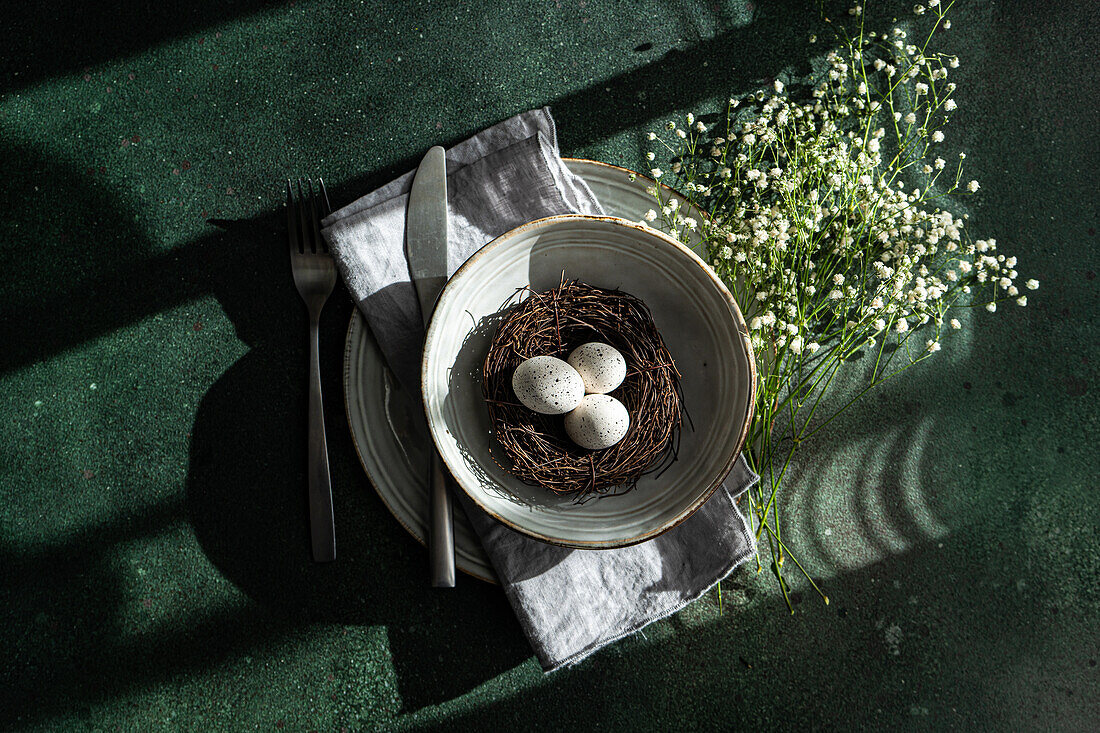 Eine elegante, frühlingshafte Tischdekoration mit einem Vogelnest mit Eiern, umgeben von zarten weißen Blumen auf einer strukturierten Oberfläche