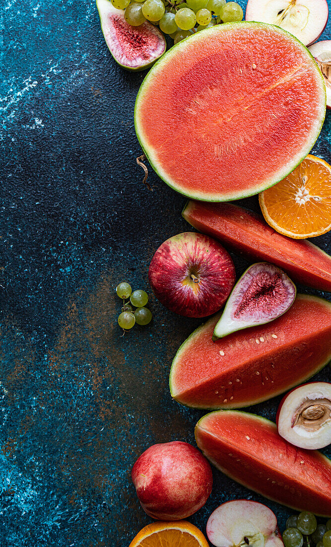 Draufsicht auf einen Rahmen mit Früchten der Saison, bestehend aus Wassermelone, Orange, Birne, Weintrauben und Äpfeln auf einer dunklen Fläche