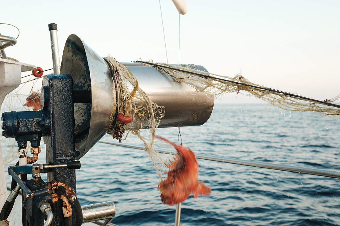 Fischerboot mit runder Trommel, die mit einem Fischernetz verschnürt ist, und hängenden roten Garnelen im Tageslicht vor dem unscharfen, sich kräuselnden blauen Meerwasser von Soller Mallorca Spanien
