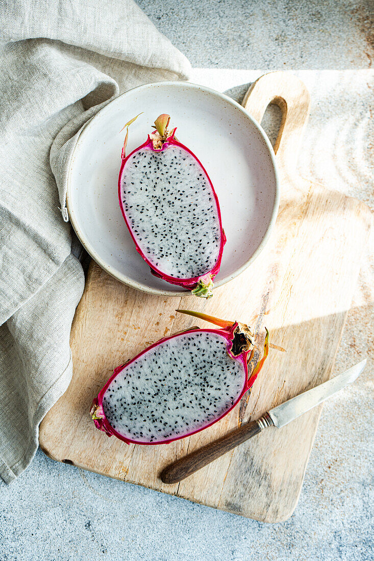 Sliced dragonfruit on a ceramic plate, displayed on a rustic wooden cutting board with a vintage knife.