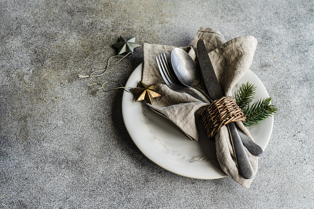 Blick von oben auf ein Vintage-Besteck mit Serviette, Löffel, Messer und Gabel auf einem Teller auf einer grauen Fläche neben Weihnachtsschmuck bei Tageslicht