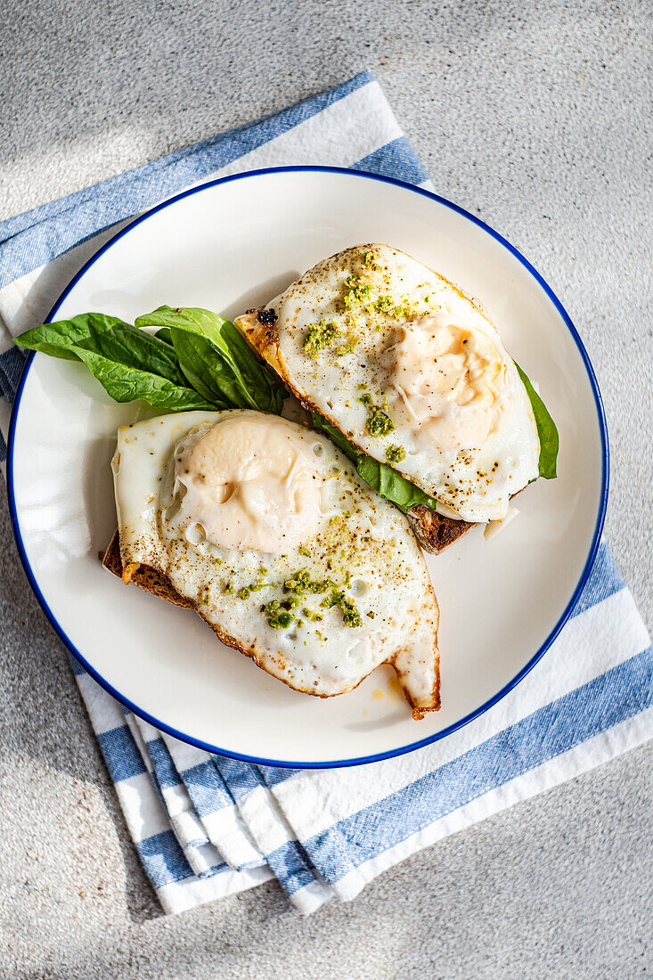 Blick von oben auf einen Teller mit appetitlichem Toast mit frischem Blattspinat, Spiegeleiern und Pestosauce auf einer blauen Serviette