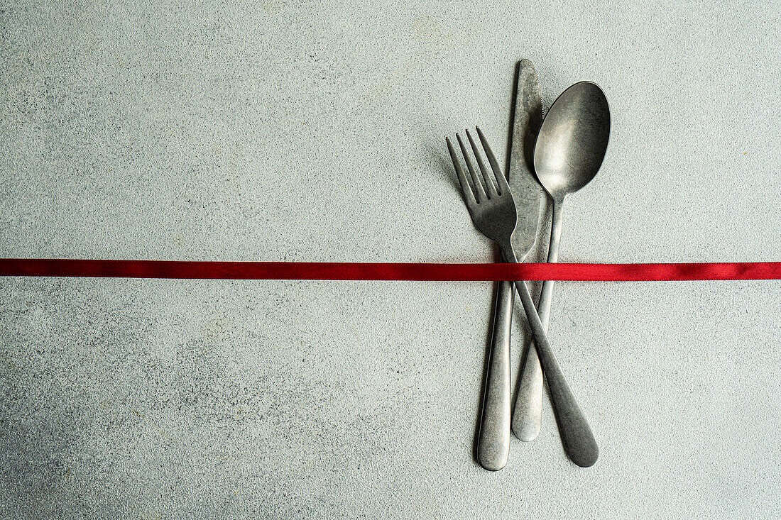 Top view of vintage cutlery set placed on gray surface with red ribbon in light kitchen