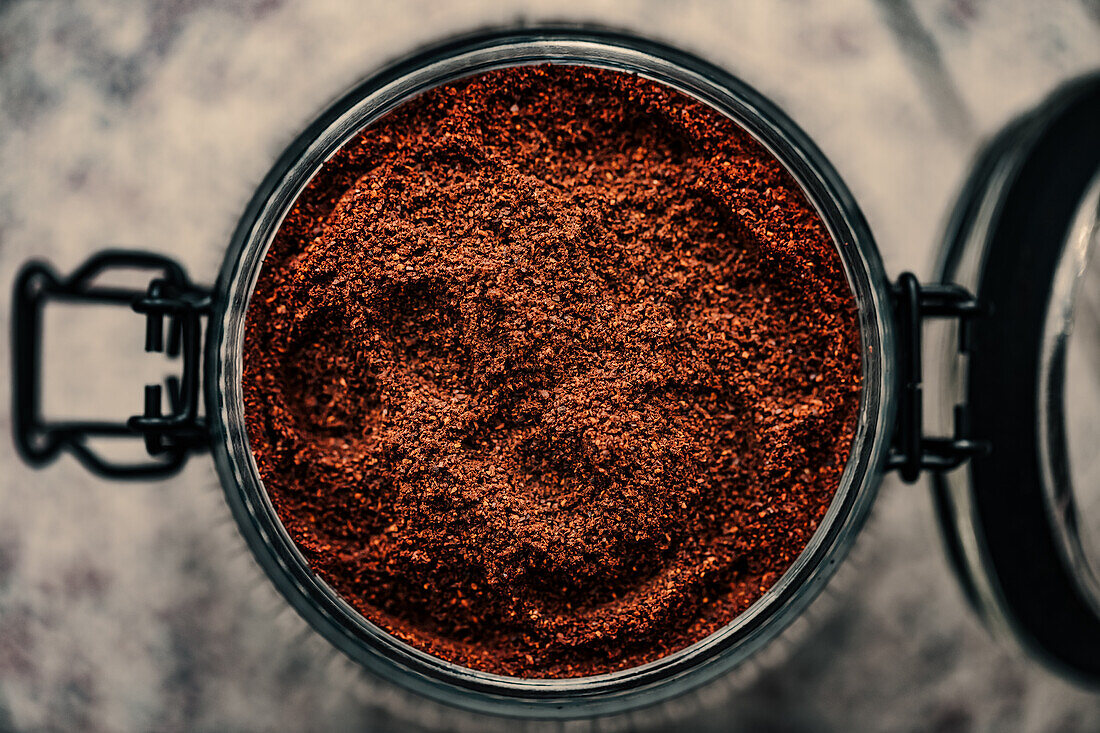 Top view of finely ground coffee filling a ribbed glass jar, highlighting its rich texture and depth, placed on a mottled background