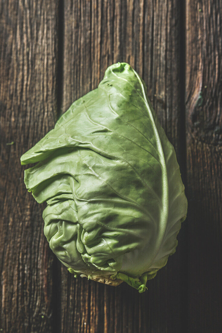 Close up of raw whole cabbage at rustic brown wooden background. Top view.