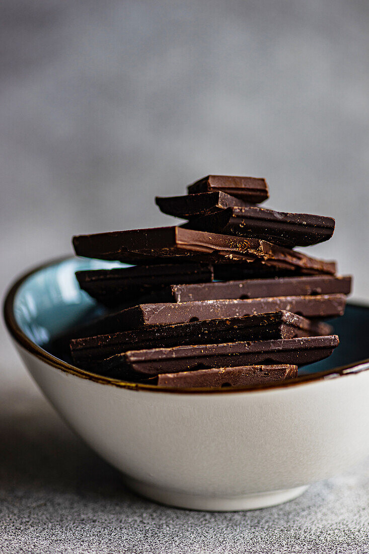 Pile of pieces of different kinds of chocolate placed in crop ceramic bowl on gray blurred table