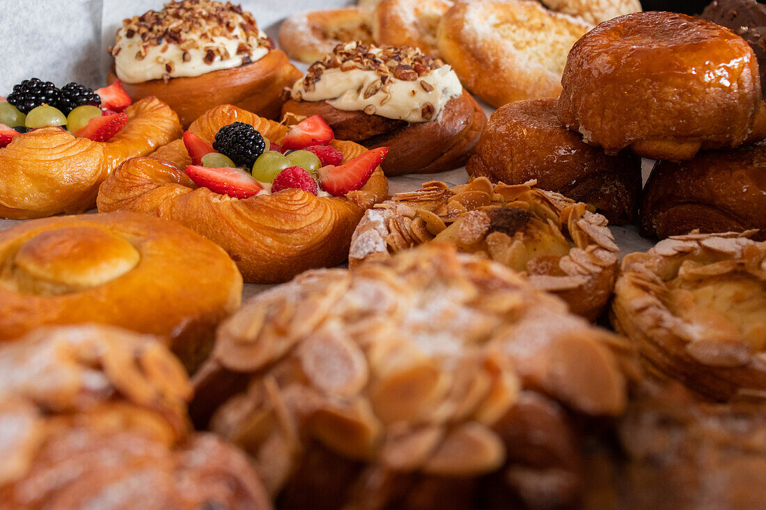 High angle closeup of assorted baked pastries with croissants and cakes with berries and cream placed on table in bakery