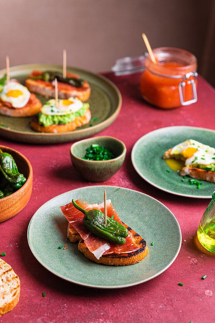 Delicious homemade Spanish tapas toasts with fried eggs, avocado and ham served on round plate near crispy bread with bacon on table