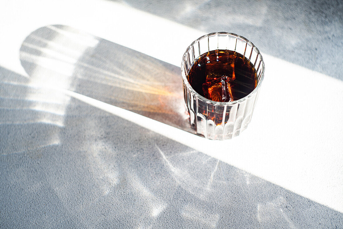 Von oben helles Sonnenlicht wirft einen lebhaften Schatten auf ein mit Kirschlikör gefülltes Glas auf einem strukturierten Tisch