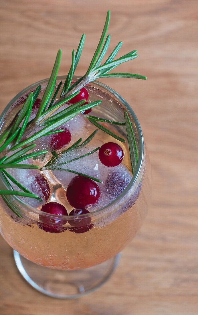 A rosemary-infused winter cocktail garnished with fresh cranberries and sprigs, served in a tall glass on a wooden surface.