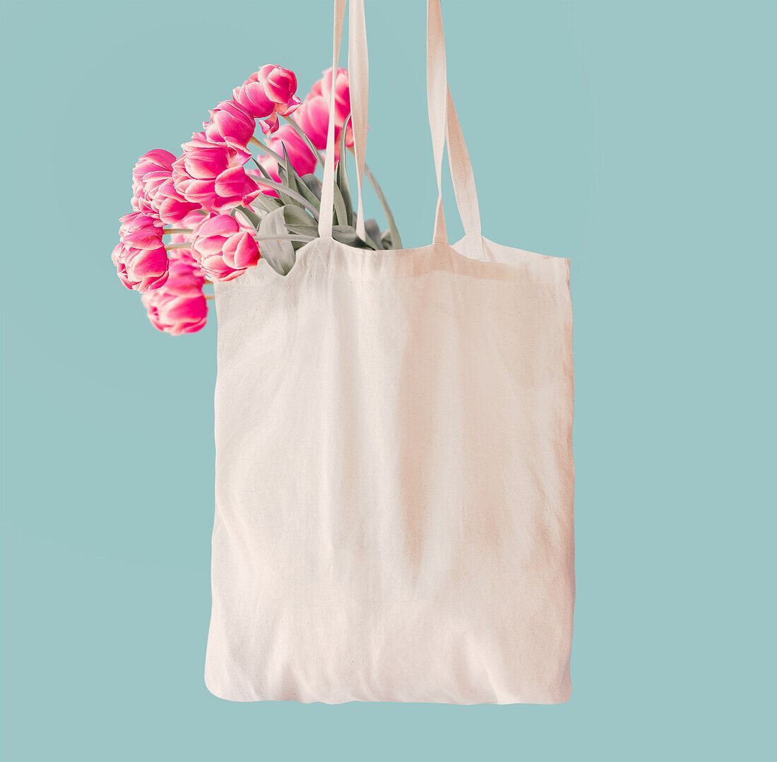 Pink tulips bunch in white cotton shopping bag with copy space at light blue wall background. Springtime concept. Zero waste