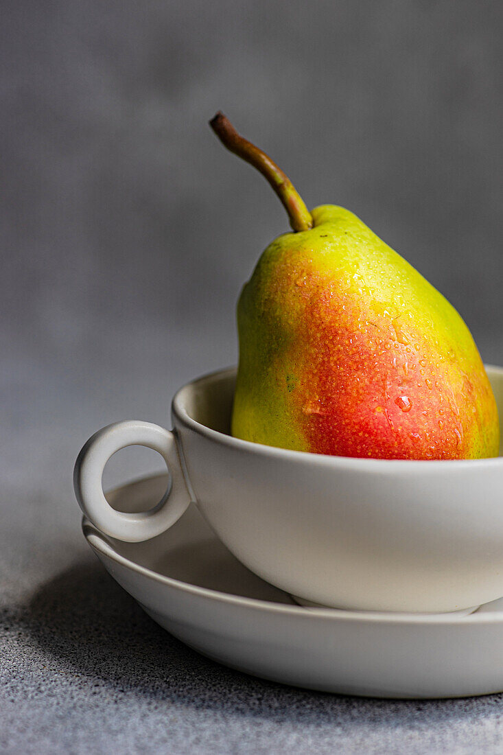 Front view of ripe organic pear fruit in cup on plate on gray blurred background