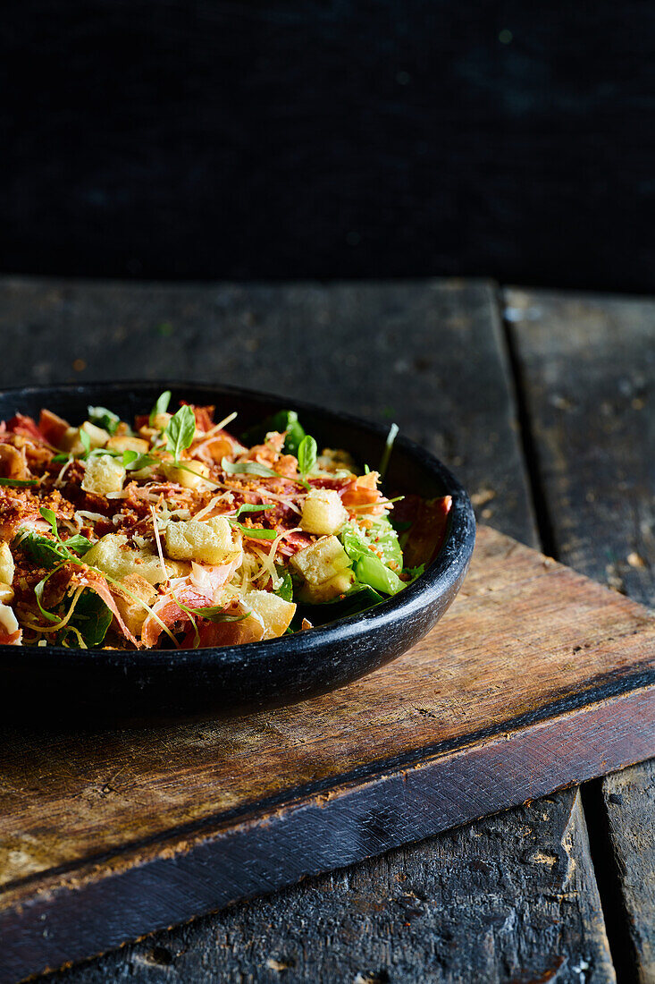 High angle of appetizing salad consisting of fresh chopped vegetables herbs and bacon served in black bowl