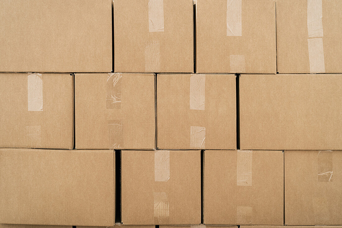 Strukturierter Hintergrund von Reihen von Kartonbehältern mit Klebebändern auf beiger Oberfläche in einem Lagerhaus