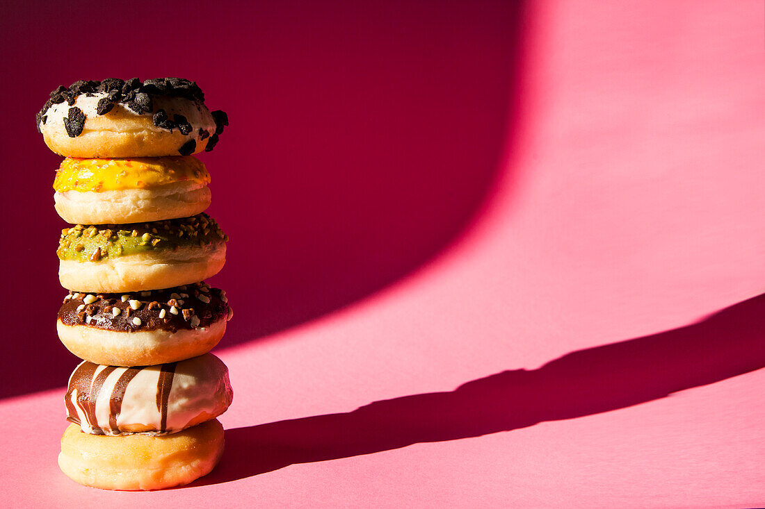 Turm von Donuts in verschiedenen Farben und Geschmacksrichtungen auf rosa Hintergrund