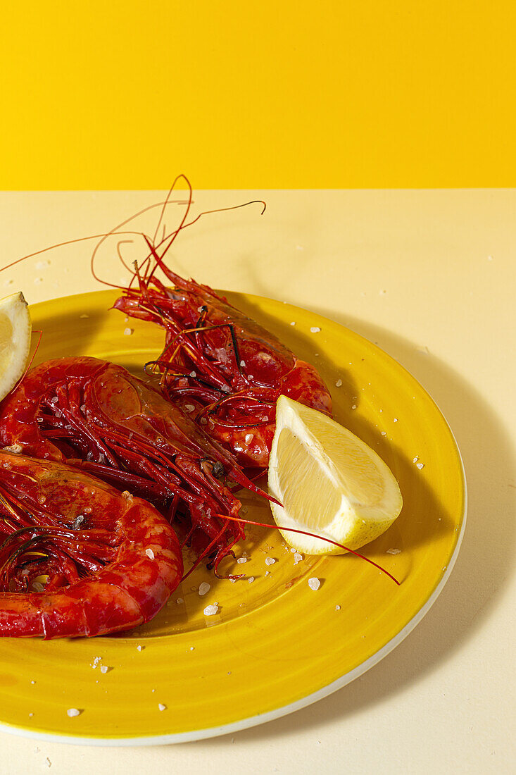 Tasty seafood of cooked red shrimps with fresh lemon slices and coarse salt on two color background