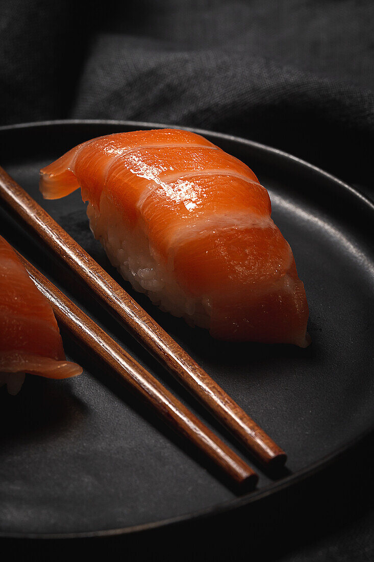 Komposition aus köstlichen frischen Sushi und Bambus-Essstäbchen, serviert auf einer schwarzen Platte auf kariertem Tuch
