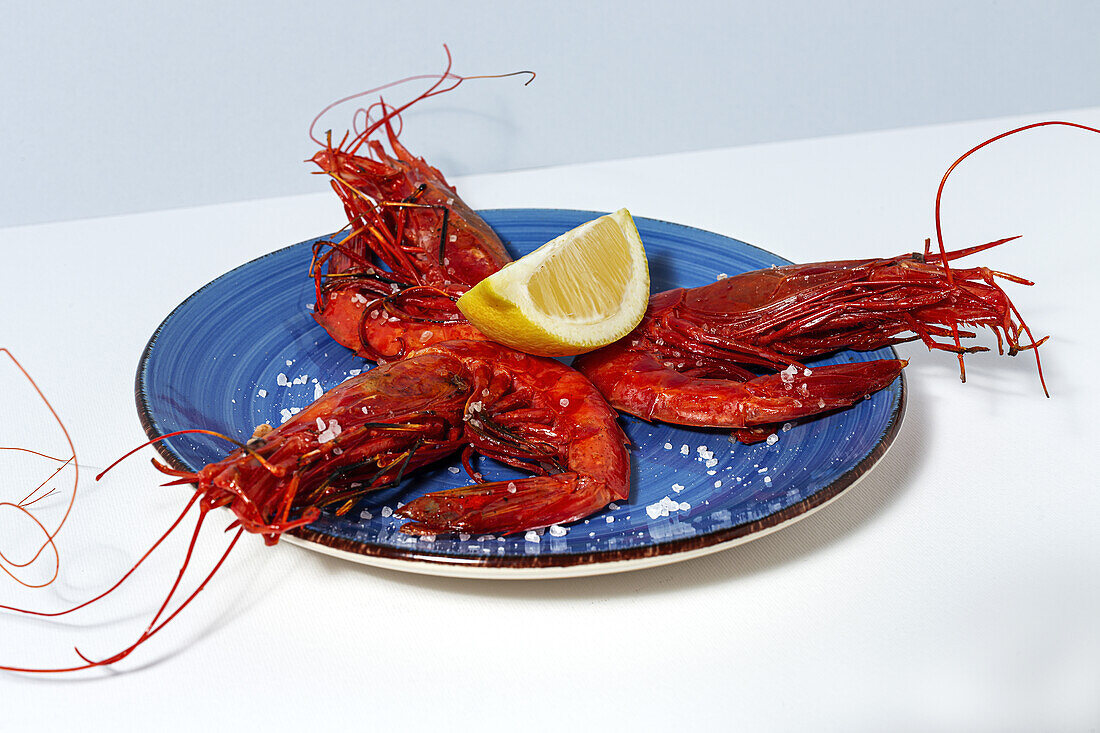 Tasty seafood of cooked red shrimps with fresh lemon slices and coarse salt on white background