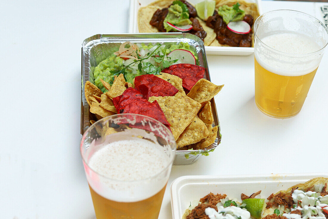 Blick von oben auf appetitliche Nachos mit Salat und Tacos mit Soße auf Tellern mit Biergläsern in einem Restaurant
