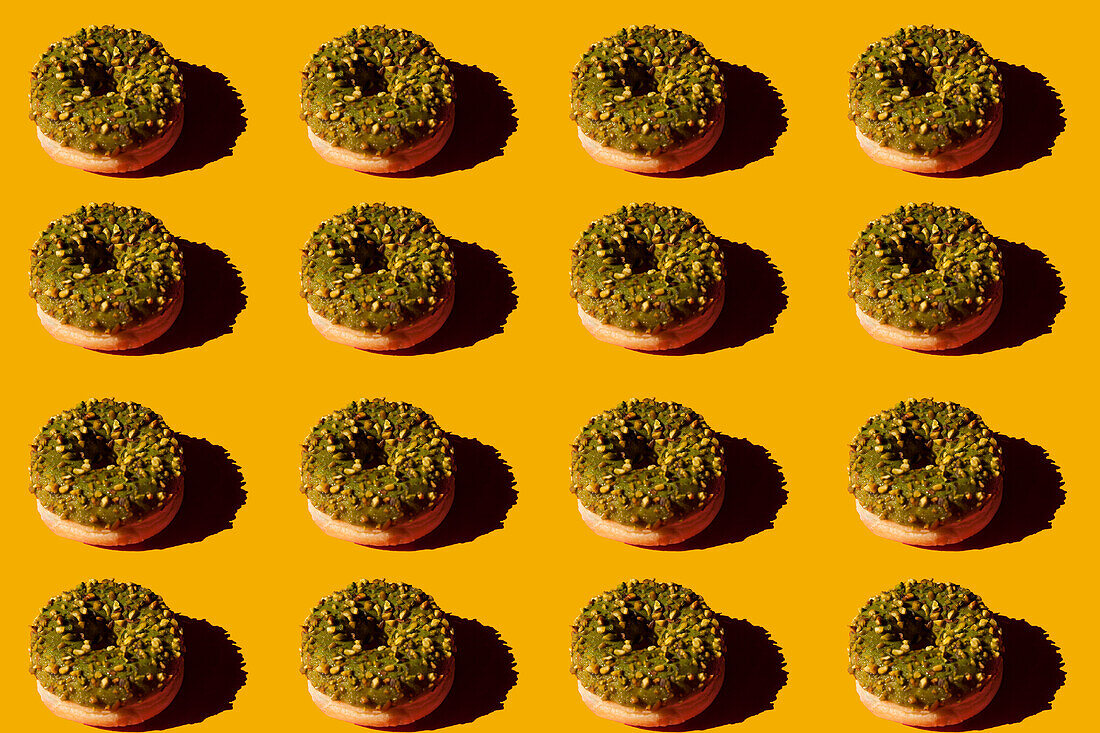 Von oben viele Donuts mit grünem Belag und Nüssen auf gelbem Hintergrund
