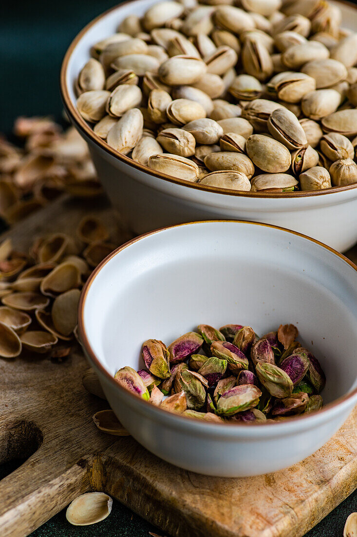 Organic and raw pistachio nuts in the bowls on green table background