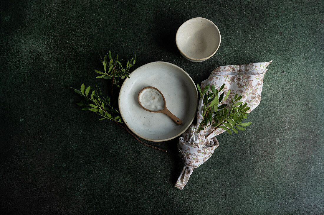 Draufsicht auf eine Tischdekoration mit einer frischen Pistazienpflanze in der Nähe von Schüsseln mit Löffel und Serviette auf einer dunkelgrauen Fläche
