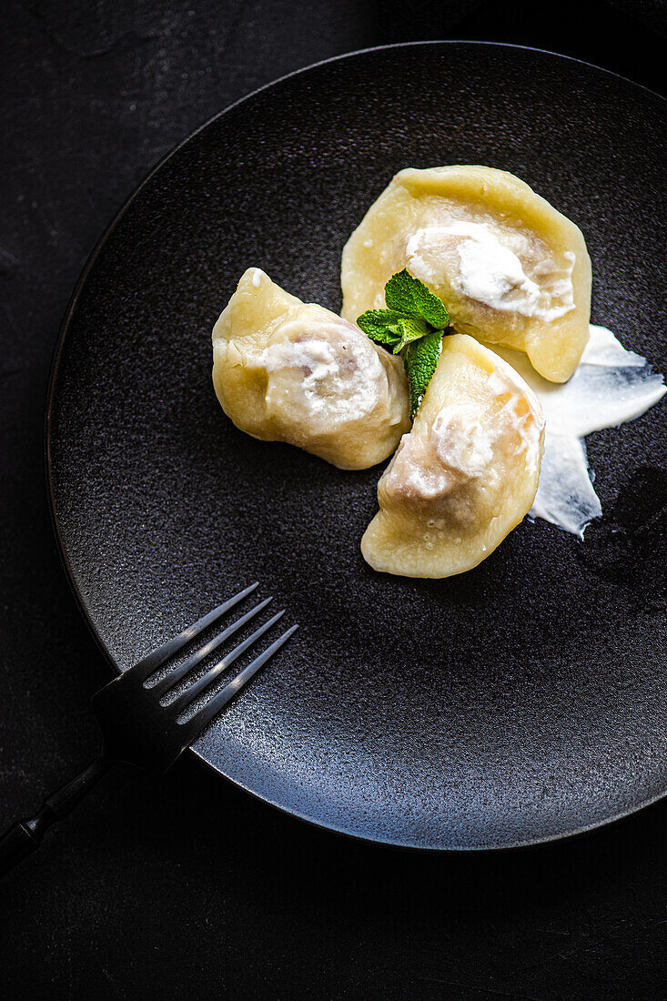 Draufsicht auf einen leckeren traditionellen ukrainischen Knödel mit Kirsche und saurer Sahne mit Minze