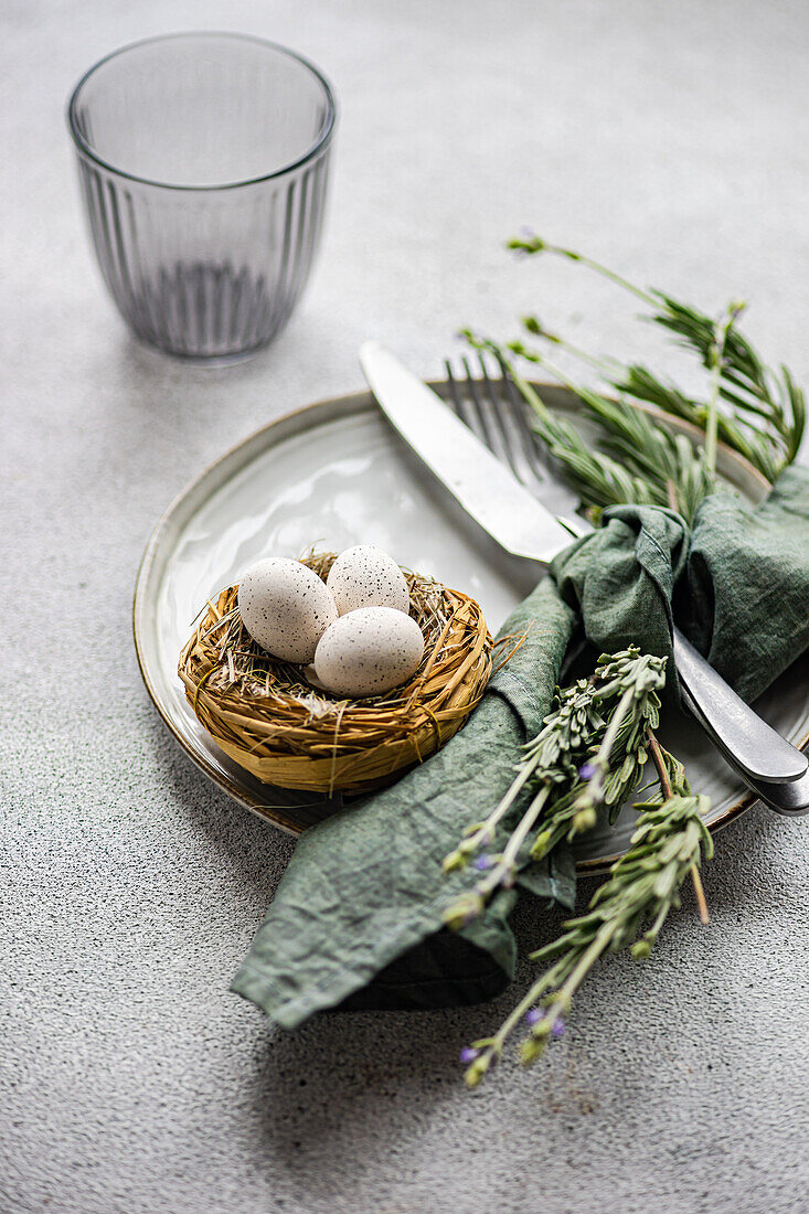 An elegant Easter table setting, featuring a small nest with speckled eggs on a ceramic plate, paired with a green napkin and lavender sprigs
