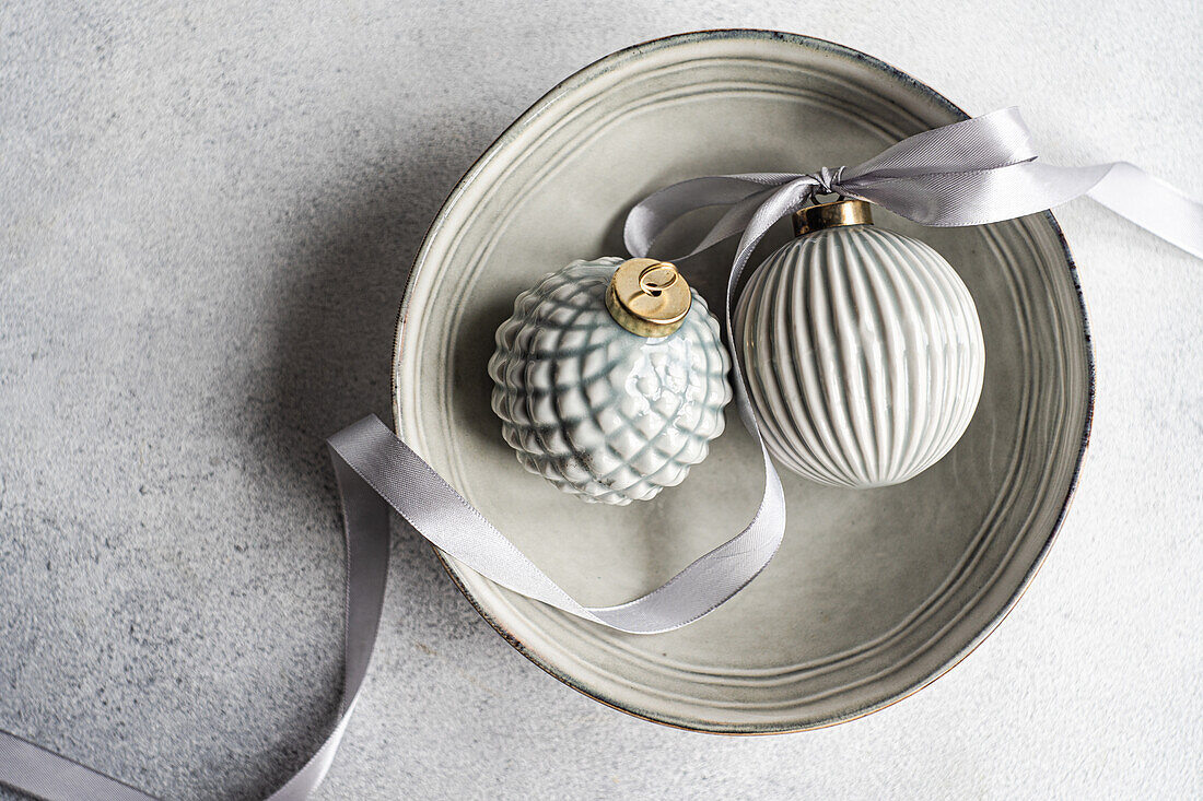 Top view of balls decorated with satin ribbon as symbol of Christmas time placed ceramic bowl on gray surface