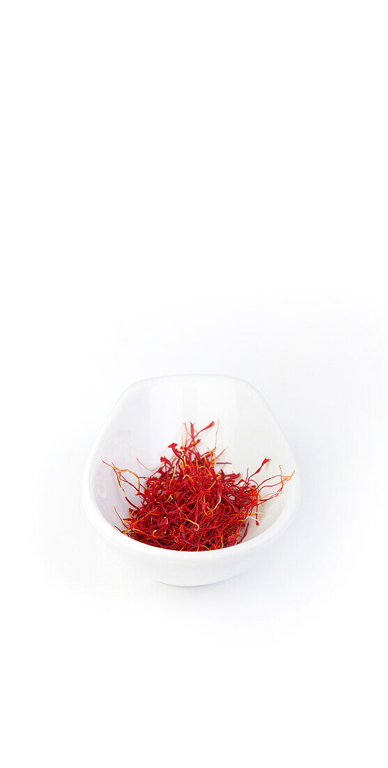 Close-up of a white bowl filled with bright red saffron threads, set against a clean white background, emphasizing the spice's rich color and texture