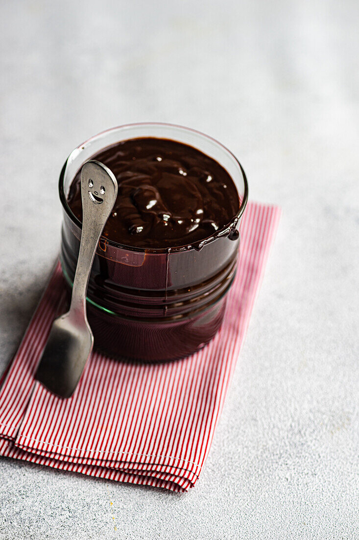 High angle of hot chocolate served in transparent glass with spoon on napkin against blurred background