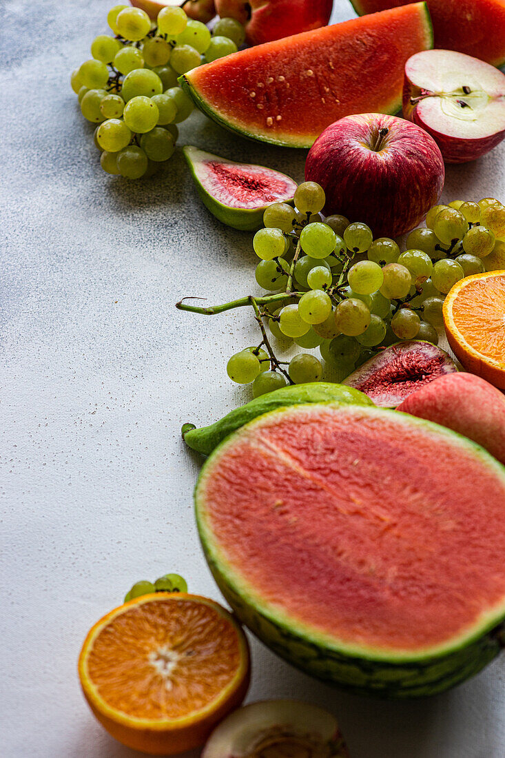 Hohe Winkel der Ernte saisonale Früchte Rahmen, bestehend aus Wassermelone, Trauben, Orangen und Äpfel auf weißer Oberfläche platziert