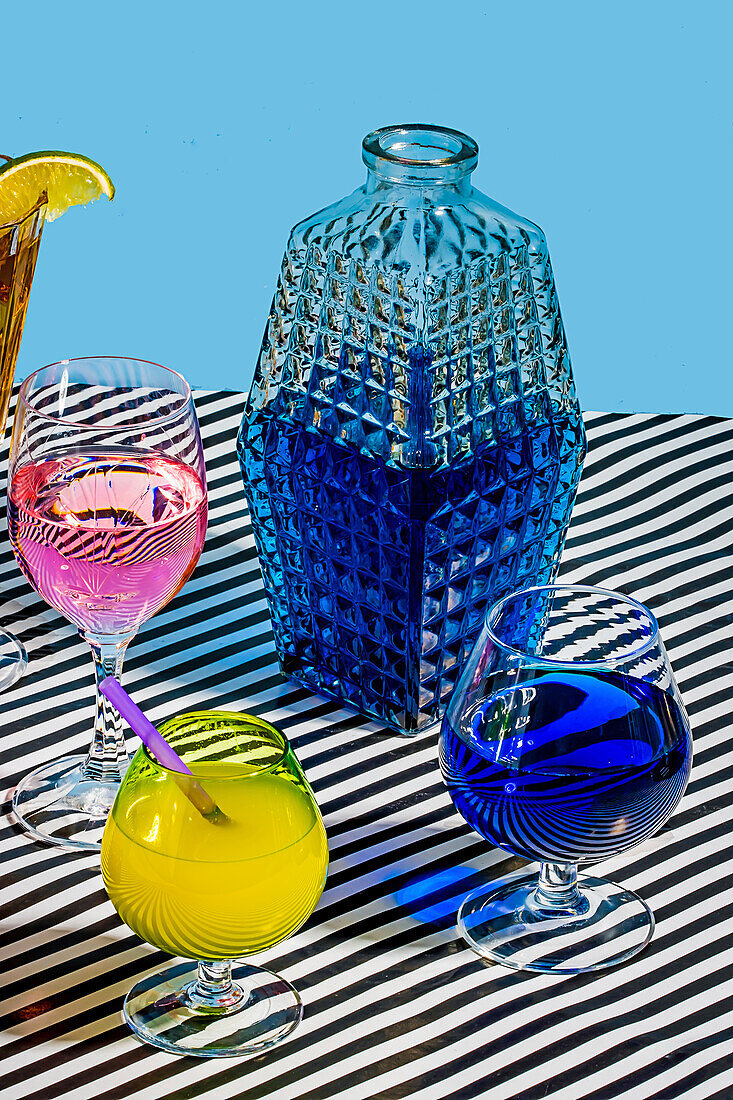 Von oben Glasgefäß mit blauer Farbe Cocktail und Sorten von bunten Getränken Long Island Iced Tea Wein Daiquiri Lemon Drop Getränk auf gestreiften Oberfläche im Licht platziert