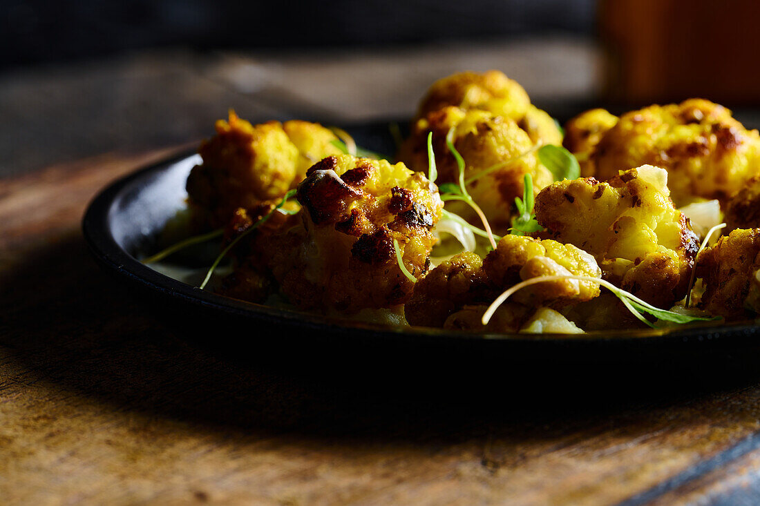 Appetizing roasted cauliflower with green herbs served on black plate placed on wooden board