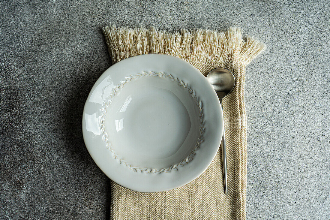 Draufsicht auf einen herbstlich gedeckten Tisch mit einer weißen Keramikschüssel neben einem Löffel auf einer Serviette auf einer grauen Fläche