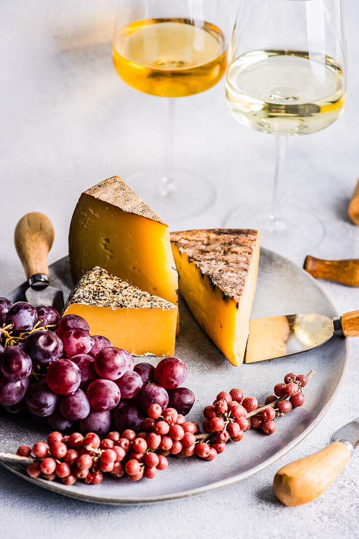 Von oben Käsevariation mit frischen Früchten auf der Steinplatte und Weißwein im Glas auf dem Betontisch
