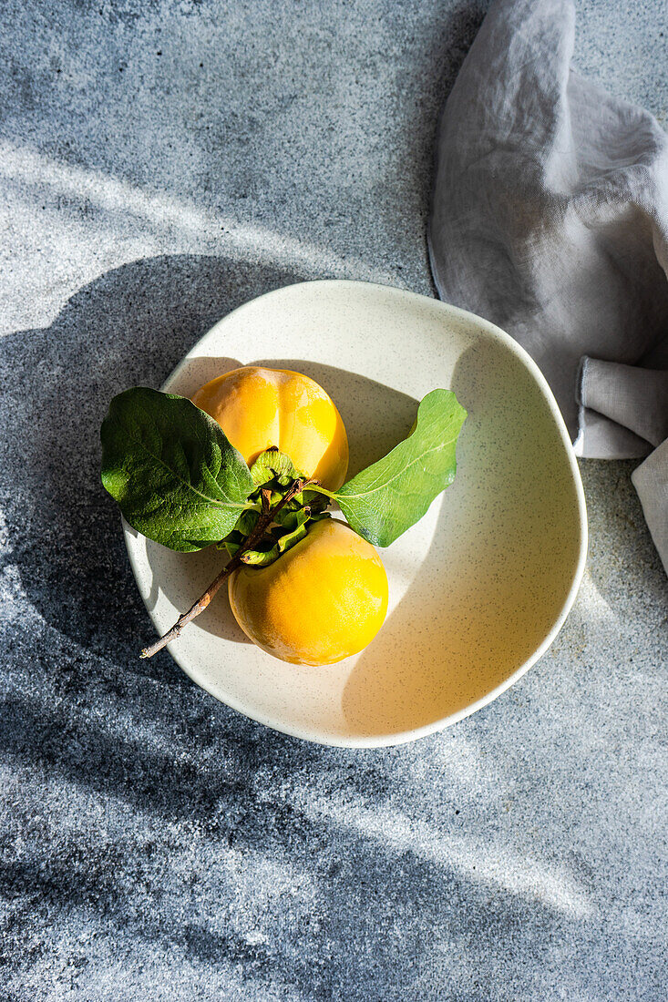 Herbstliches Gedeck mit frischen, reifen Kakifrüchten auf einem Betontisch von oben